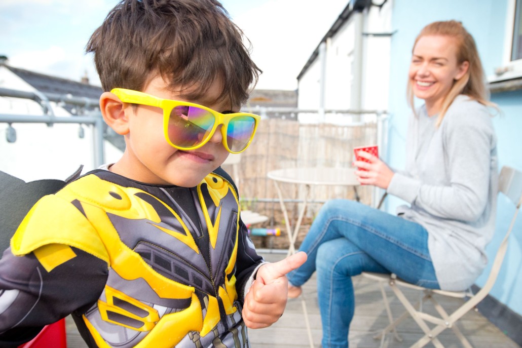 Image of women laughing at child with fancy dress costume on and glasses.