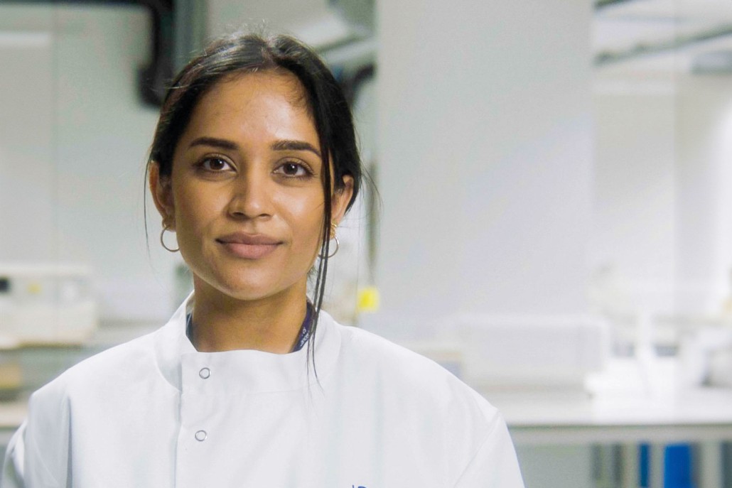 A scientist in a white lab coat looking at the camera.