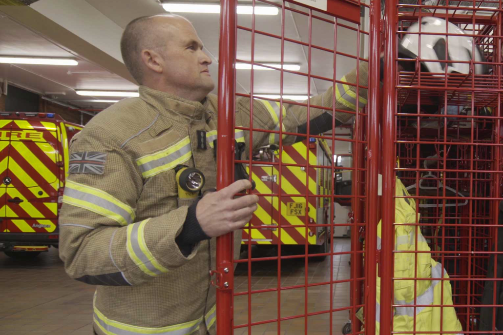 Image of a fireman inside a fire station, reaching to collect his fire helmet.