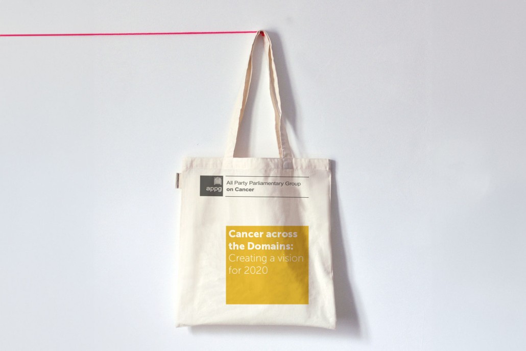 A tote bag hanging up with a yellow square and the words 'Cancer across the domains: Creating a vision for 2020.